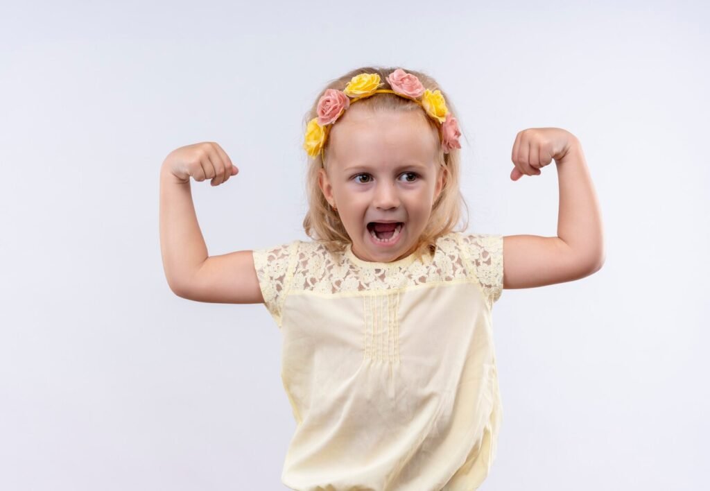 jolie petite fille portant chemise jaune bandeau floral montrant ses muscles mur blanc 141793 32488