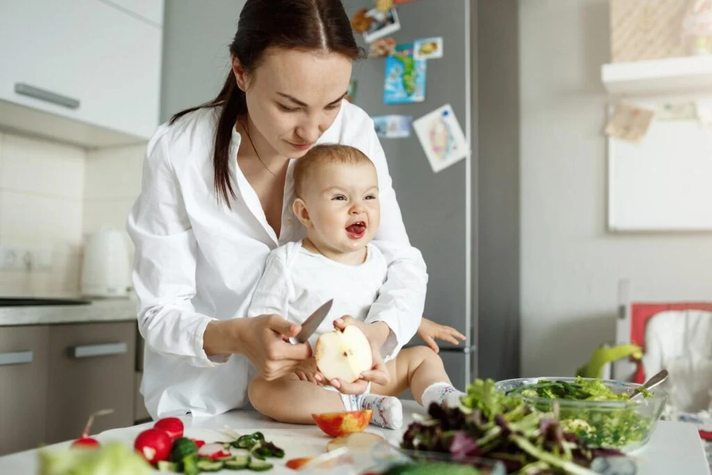 Bébé assis à table pendant que sa maman prépare une salade pour le déjeuner